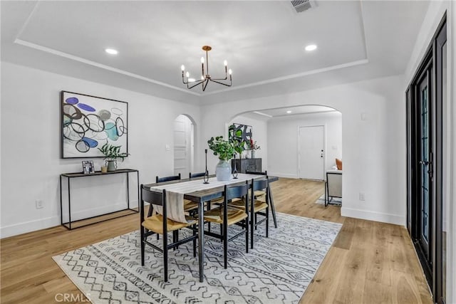 dining space featuring arched walkways, a notable chandelier, visible vents, light wood-type flooring, and a tray ceiling