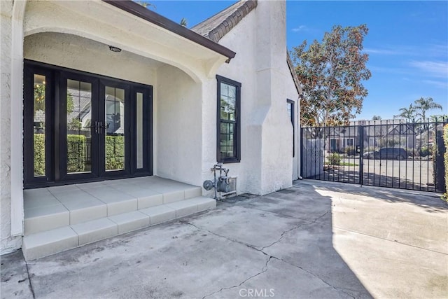 entrance to property featuring french doors, fence, and stucco siding