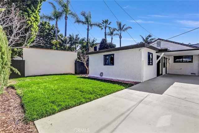 view of side of home featuring driveway, fence, a lawn, and stucco siding