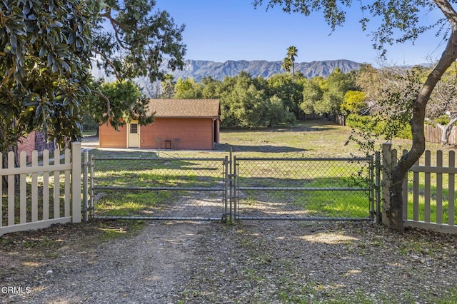 view of gate featuring a mountain view, fence, and a lawn