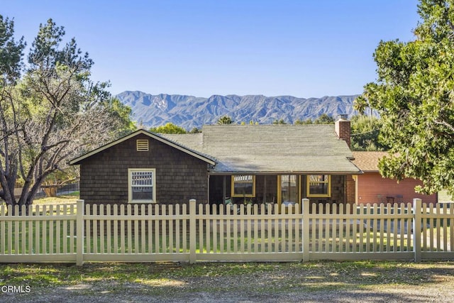 ranch-style home featuring a fenced front yard, a chimney, a mountain view, and a porch