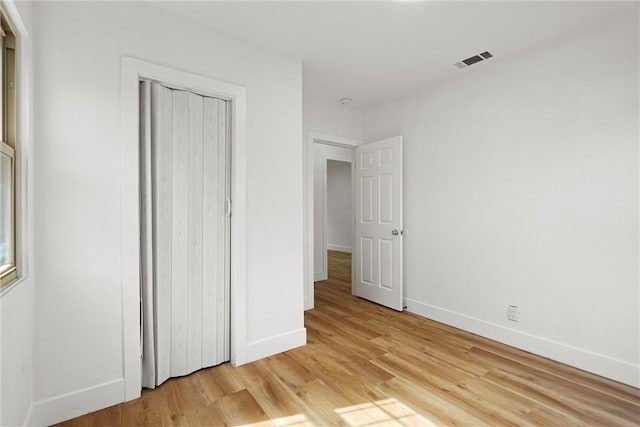 unfurnished bedroom featuring light wood-type flooring, baseboards, visible vents, and a closet