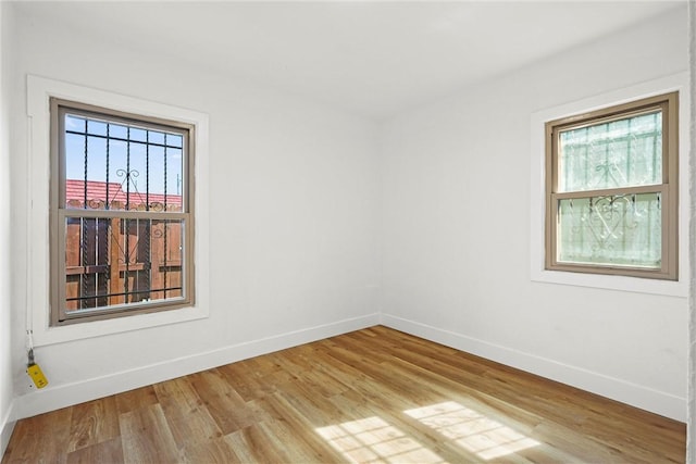 empty room featuring light wood finished floors, a wealth of natural light, and baseboards