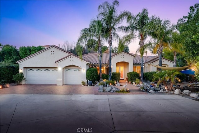 mediterranean / spanish house featuring decorative driveway, a tiled roof, an attached garage, and stucco siding