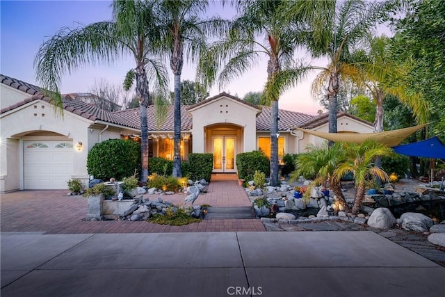 mediterranean / spanish home featuring a tiled roof, french doors, decorative driveway, and an attached garage