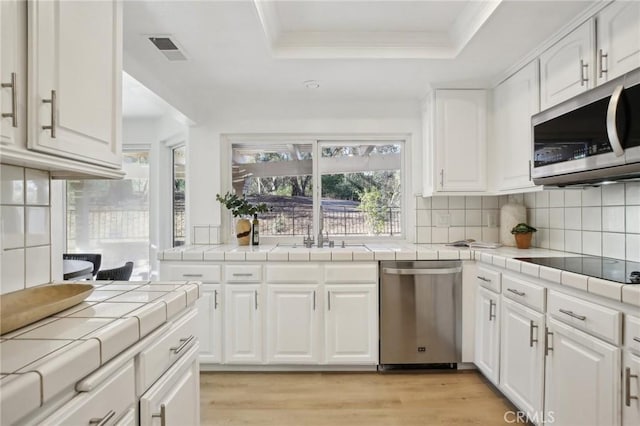 kitchen featuring appliances with stainless steel finishes, tile counters, a raised ceiling, and decorative backsplash