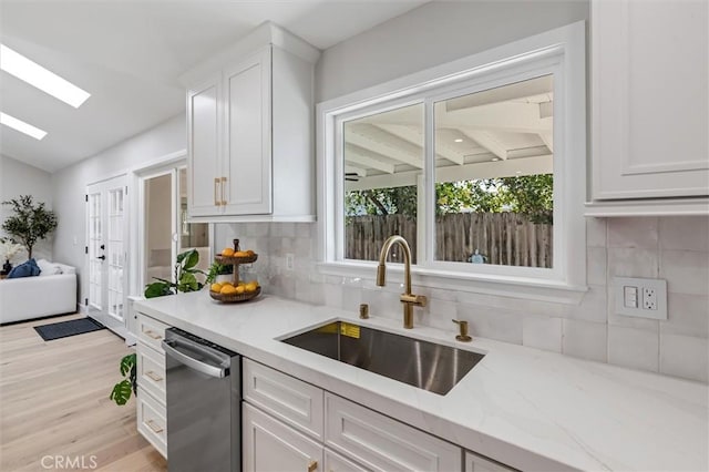 kitchen featuring white cabinets, a sink, stainless steel dishwasher, and light stone countertops