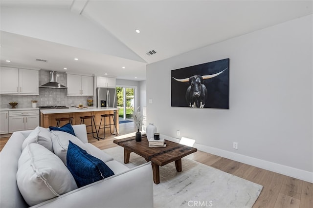 living room with high vaulted ceiling, light wood-style flooring, visible vents, and baseboards