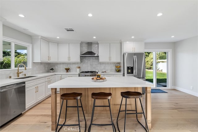 kitchen with visible vents, a center island, stainless steel appliances, wall chimney range hood, and a sink