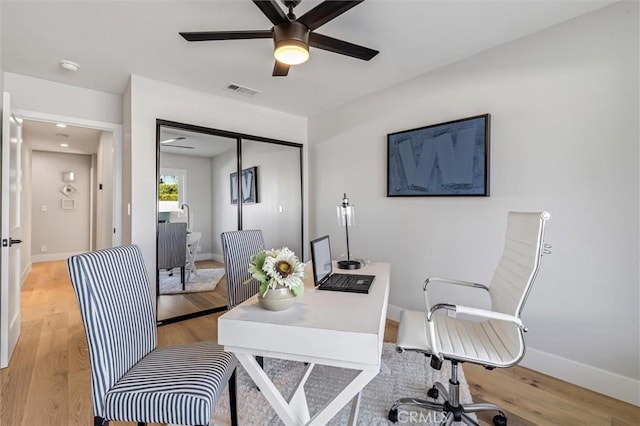 office space featuring light wood finished floors, a ceiling fan, visible vents, and baseboards