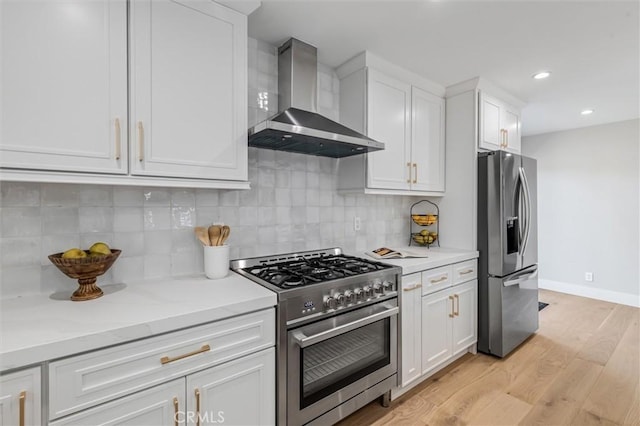 kitchen with tasteful backsplash, appliances with stainless steel finishes, light wood-style floors, white cabinets, and wall chimney exhaust hood