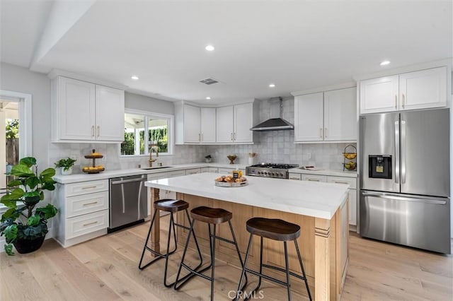 kitchen with a breakfast bar, a sink, visible vents, appliances with stainless steel finishes, and wall chimney exhaust hood