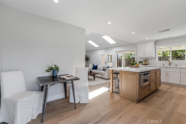 kitchen with light wood-style flooring, stainless steel oven, visible vents, and white cabinets