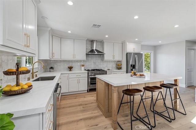 kitchen featuring a breakfast bar area, stainless steel appliances, visible vents, a sink, and wall chimney exhaust hood