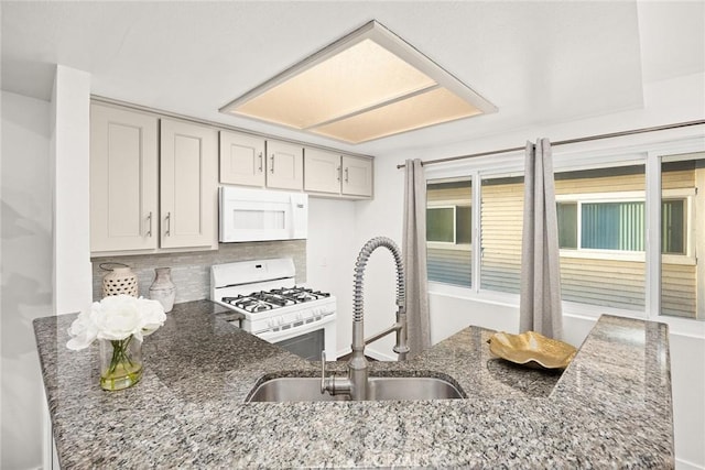 kitchen featuring dark stone counters, white appliances, a sink, and decorative backsplash