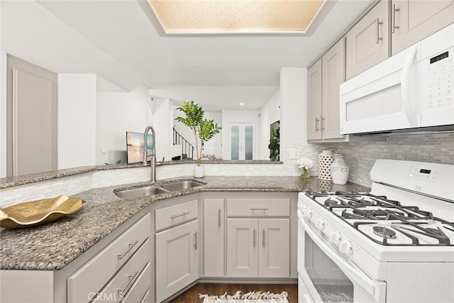 kitchen with white appliances, decorative backsplash, light stone countertops, white cabinetry, and a sink