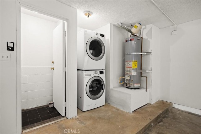 laundry area featuring a textured ceiling, laundry area, stacked washer / drying machine, water heater, and concrete block wall