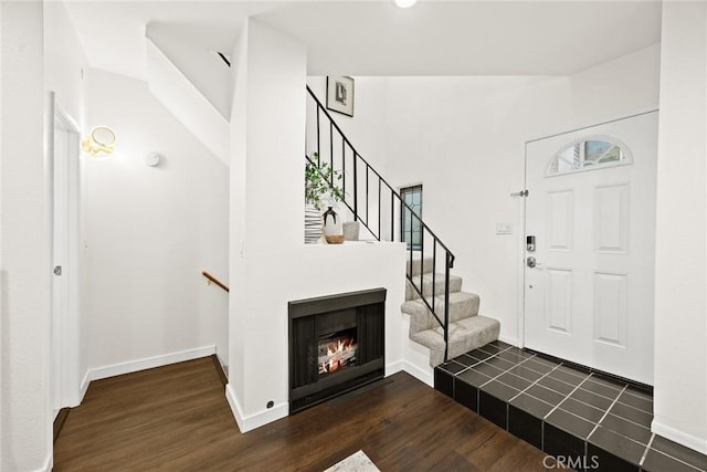 entrance foyer featuring dark wood-style floors, a lit fireplace, stairway, and baseboards