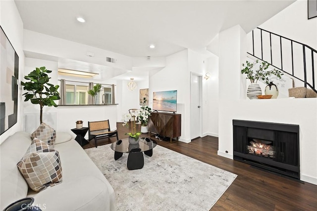 living area featuring recessed lighting, visible vents, wood finished floors, a warm lit fireplace, and baseboards