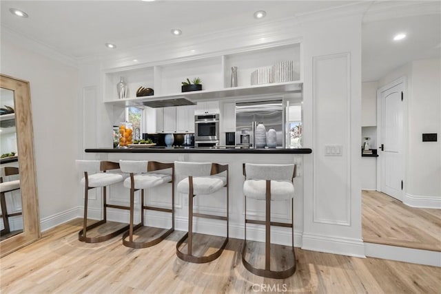 bar featuring ornamental molding, built in refrigerator, recessed lighting, and light wood-style floors