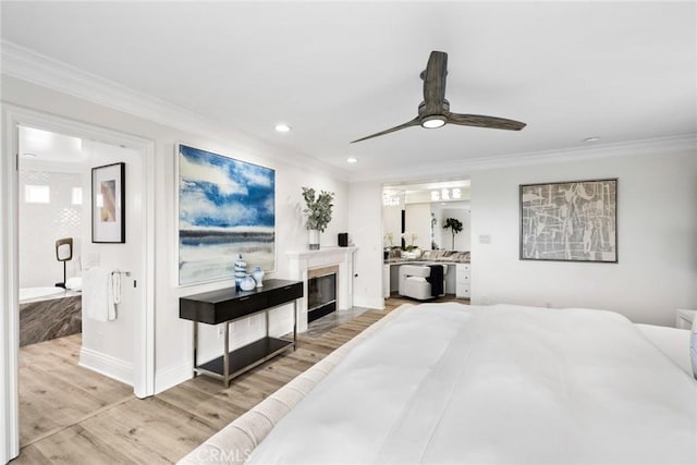 bedroom featuring light wood-style floors, ornamental molding, ensuite bathroom, and a glass covered fireplace