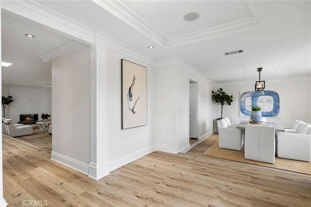 hall with visible vents, baseboards, light wood-style floors, ornamental molding, and a tray ceiling