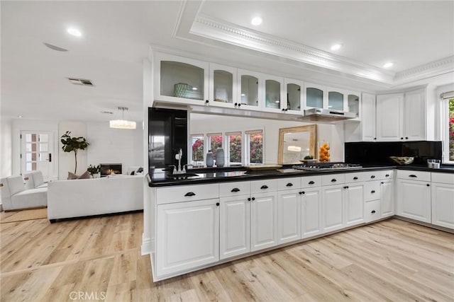 kitchen with a tray ceiling, stainless steel gas cooktop, dark countertops, visible vents, and a warm lit fireplace