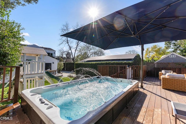 wooden terrace with hot tub deck surround, a fenced backyard, and an outdoor structure