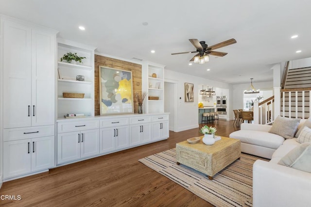 living area with ceiling fan with notable chandelier, recessed lighting, stairway, and wood finished floors