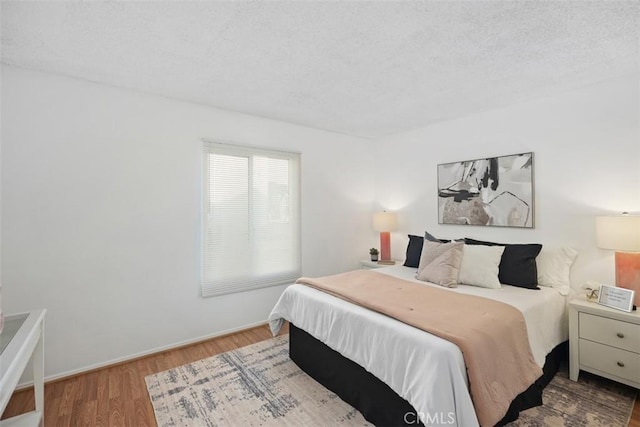 bedroom with a textured ceiling, baseboards, and wood finished floors