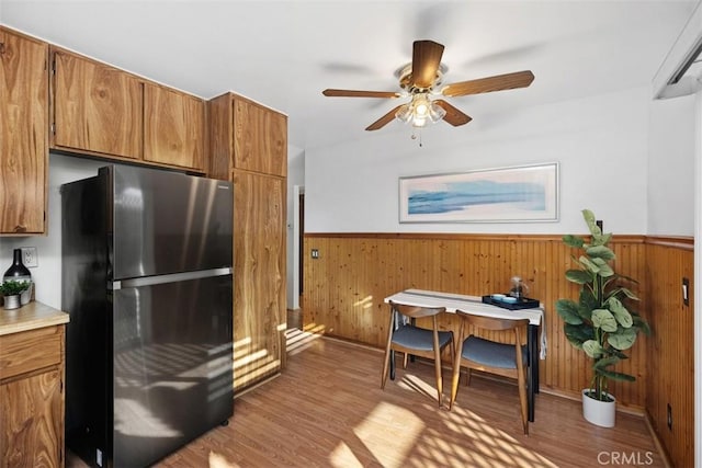 kitchen featuring wainscoting, brown cabinetry, wood finished floors, and freestanding refrigerator