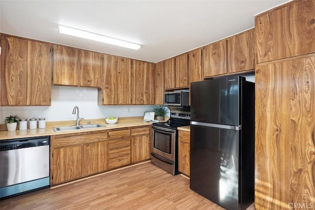 kitchen with stainless steel appliances, light countertops, brown cabinetry, a sink, and light wood-type flooring