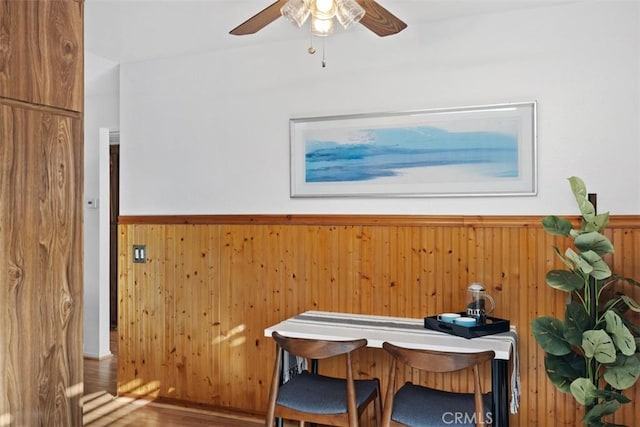 interior space with wooden walls, a ceiling fan, wood finished floors, and wainscoting