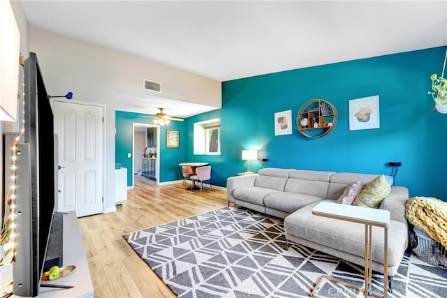 living room with an accent wall, visible vents, baseboards, and wood finished floors