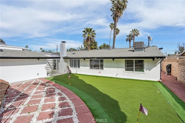 rear view of house featuring a chimney, stucco siding, a shingled roof, central AC unit, and fence