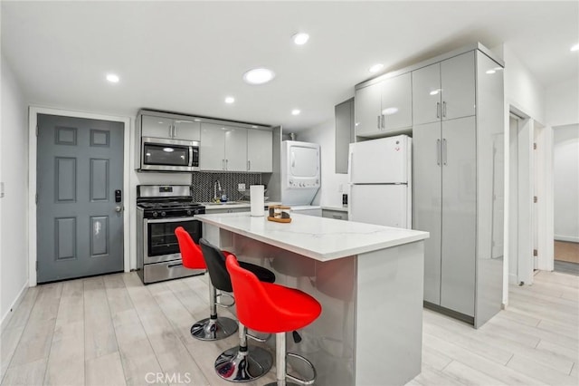 kitchen featuring stacked washer and dryer, a center island, appliances with stainless steel finishes, and gray cabinetry