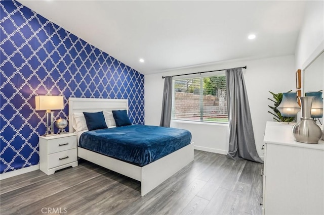 bedroom with wallpapered walls, an accent wall, baseboards, and wood finished floors