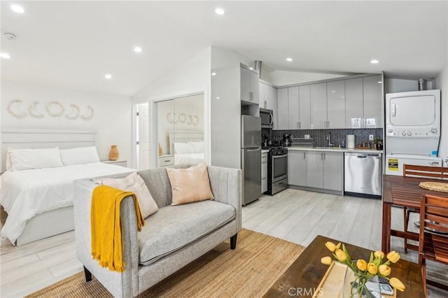 kitchen featuring vaulted ceiling, stainless steel appliances, gray cabinets, and stacked washer / drying machine