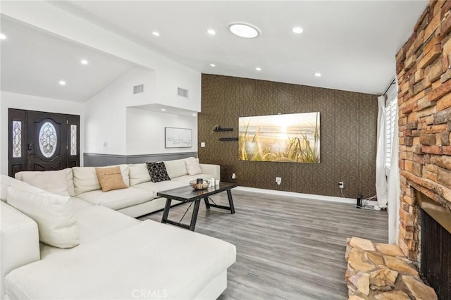 living room with lofted ceiling, a stone fireplace, visible vents, and recessed lighting