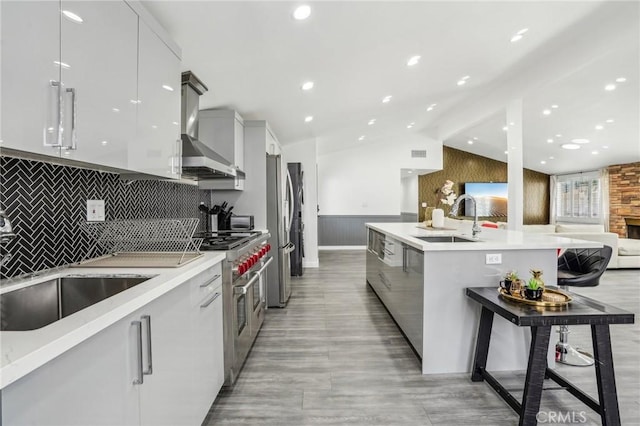 kitchen featuring lofted ceiling, modern cabinets, stainless steel appliances, wall chimney range hood, and a sink