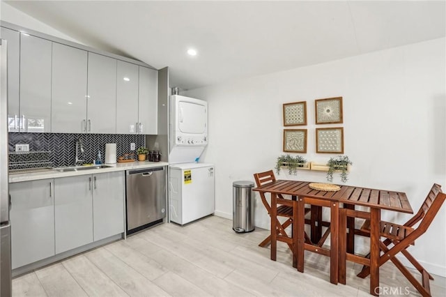 kitchen featuring stacked washer and dryer, decorative backsplash, gray cabinets, light countertops, and stainless steel dishwasher