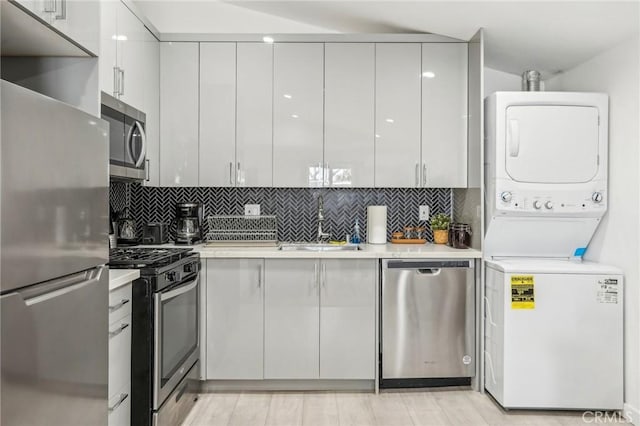 kitchen with modern cabinets, stainless steel appliances, stacked washer / drying machine, and light countertops