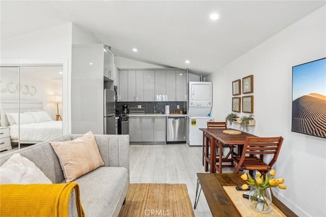 kitchen featuring modern cabinets, stacked washer / drying machine, vaulted ceiling, stainless steel appliances, and gray cabinetry