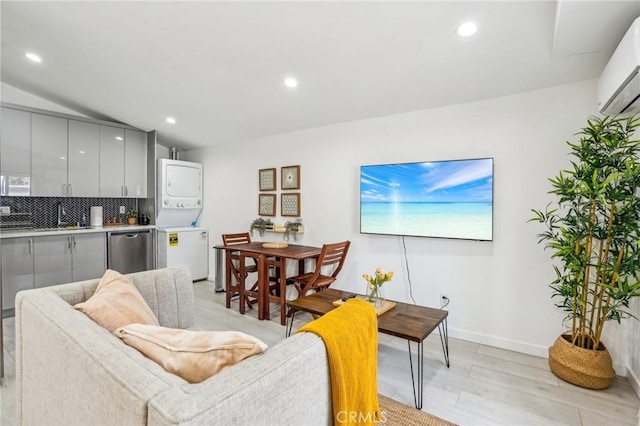 living area with a wall mounted AC, recessed lighting, vaulted ceiling, and stacked washer and clothes dryer