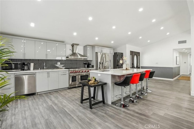 kitchen featuring visible vents, wall chimney range hood, appliances with stainless steel finishes, modern cabinets, and a kitchen bar