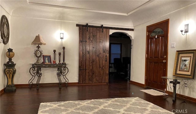 hallway with arched walkways, a barn door, wood finished floors, and baseboards