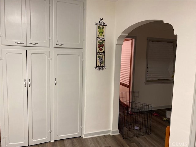 hallway with dark wood-type flooring, arched walkways, and baseboards