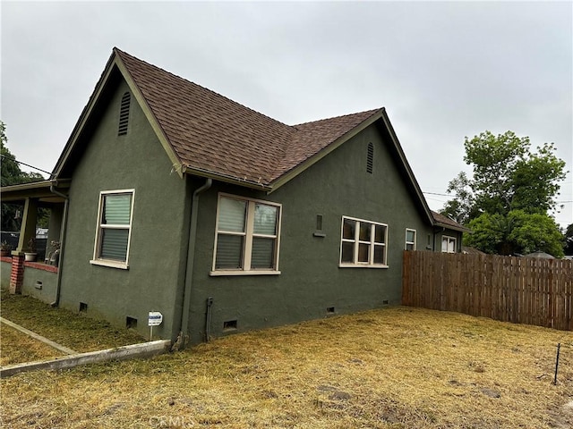 view of side of property with roof with shingles, crawl space, fence, and stucco siding