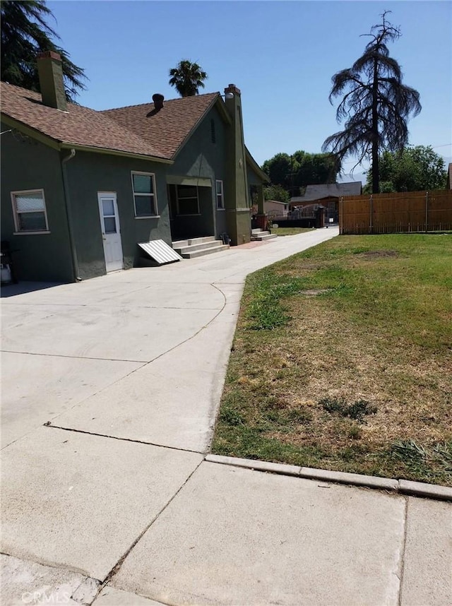 view of side of home with a yard, a chimney, fence, and stucco siding