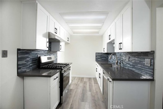 kitchen featuring stainless steel appliances, dark countertops, a sink, and under cabinet range hood